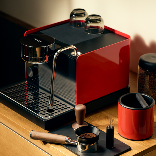 A red Fellow Espresso Series 1 with pressure control and cups sits on a wooden counter.